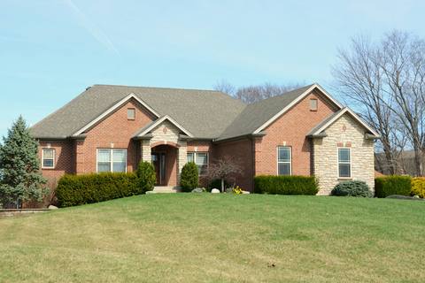 A brick house behind a wide, freshly mown green lawn under a clear blue sky.