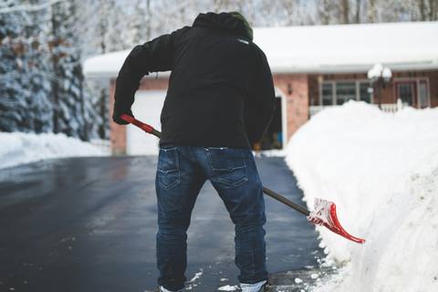 A person clearing a snow-covered driveway with a shovel in front of a house.